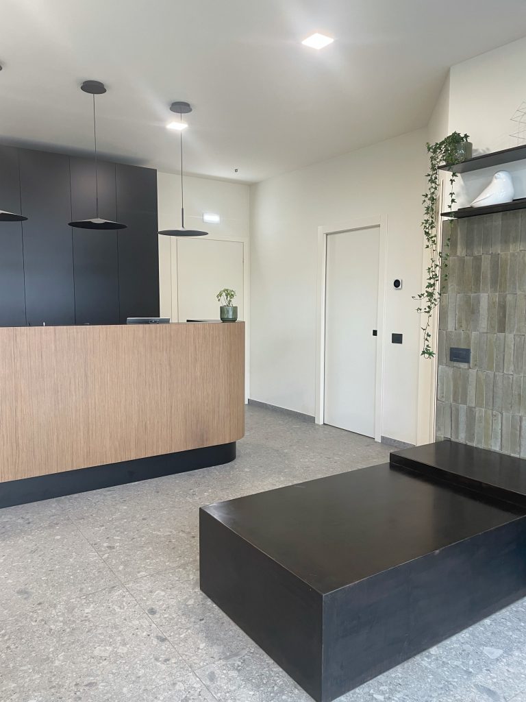 Studio veterinario: reception curva in legno chiaro con pareti scure, pavimento in terrazzo e piastrelle verdi